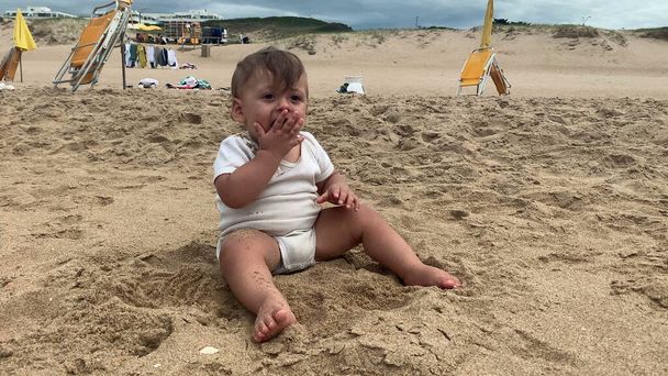 Дитина їсть пісок на пляжі, малюк кладе пісок в рот
 - Фото, зображення