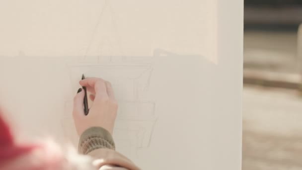 鉛筆で屋外のキャンバスにタワーを描くピンク髪の少女の肩の上に - 映像、動画