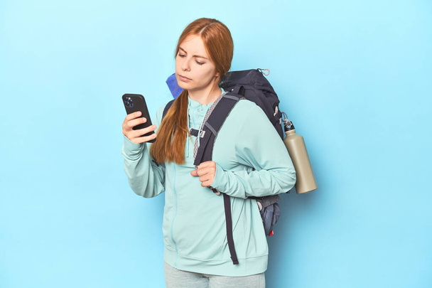 Redhead mountaineer with adventure backpack in blue studio - Photo, Image