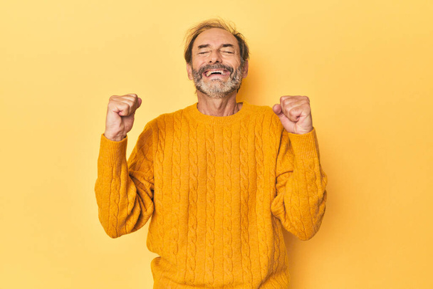 Hombre caucásico de mediana edad en estudio amarillo celebrando una victoria, pasión y entusiasmo, expresión feliz. - Foto, imagen