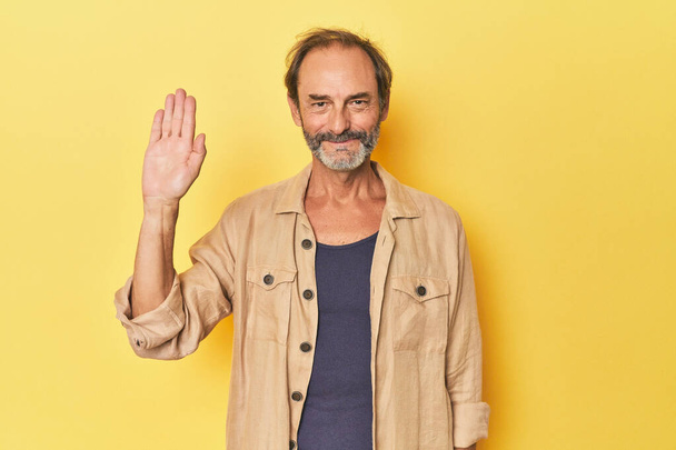Fehér középkorú férfi sárga stúdióban vidám mosollyal mutatja az ötös számú ujjaival. - Fotó, kép