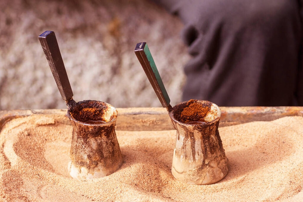 Traditional turkish coffee prepared on hot sand.. Two cezves filled with hot oriental coffee. Two potons for preparation of coffee. jezveh. jezve. - Photo, Image