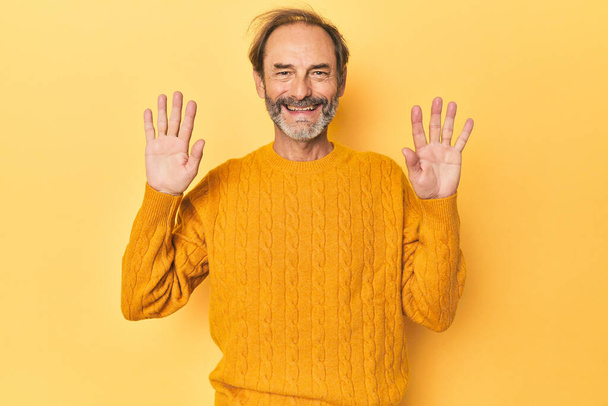 Kaukasischer Mann mittleren Alters im gelben Studio, der die Nummer zehn mit den Händen zeigt. - Foto, Bild