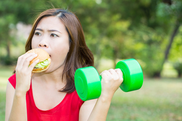 Азиатка ест гамбургер с тяжелой атлетикой
 - Фото, изображение