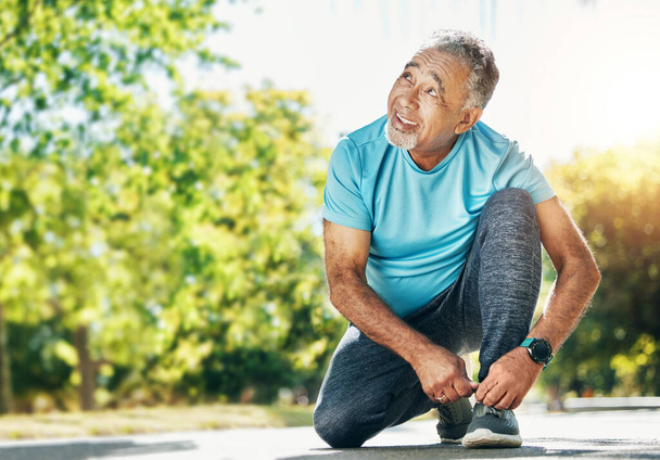 Tying laces, man and in a park for running, exercise and getting ready for outdoor cardio. Smile, idea and a mature or senior male athlete with shoes in the street for a workout, exercise or training. - Photo, Image