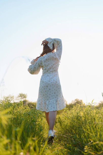 Обратный вид женщины в белом платье в поле на закате - Фото, изображение