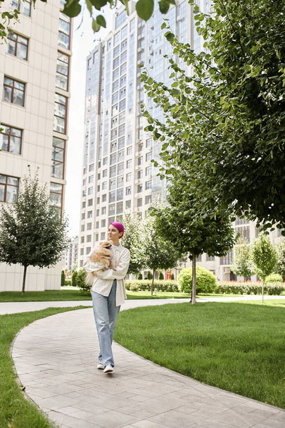 volle Länge der stilvollen Frau mit kleinem reinrassigen Hund in den Händen, der auf der Straße spaziert, Stadtleben - Foto, Bild