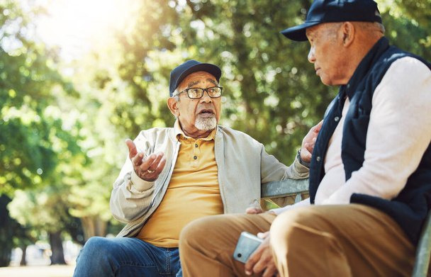 Senioren, mannen en conversatie op parkbank, binding maken en ontspannen buiten met telefoon. Ouderen die 's morgens samen in de tuin, in de communicatie en in de natuur zitten om met pensioen te gaan. - Foto, afbeelding