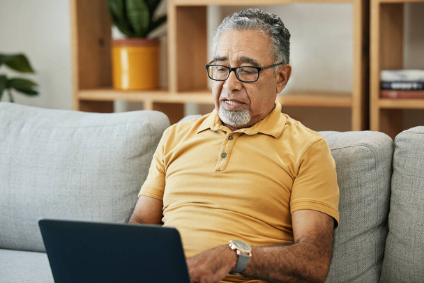 Пенсионер, сидящий на диване дома с онлайн-исследованиями в гостиной или потоковым видео, фильмами или телешоу. Пожилые люди, человек или писать на компьютере в отставке для блога или общения. - Фото, изображение