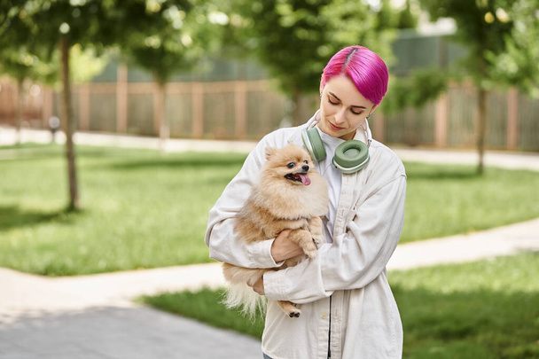 loving pet owner with purple hair and headphones walking with loveable pomeranian spitz in hands - Valokuva, kuva