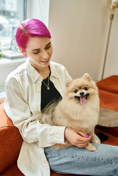 smiling purple-haired woman sitting with funny pomeranian spitz in modern dog hotel, pet service - Fotó, kép