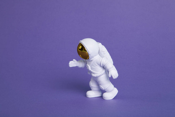 una statuetta astronauta in tuta spaziale che esplora uno sfondo viola. Fotografia colorata di nature morte creativa minimale - Foto, immagini