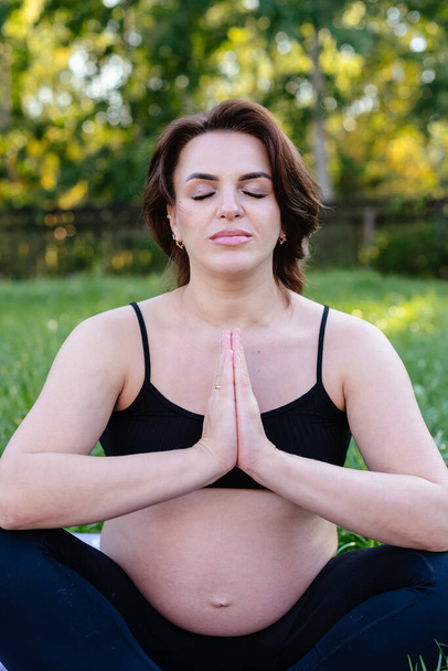 Schwangere machen Yoga und meditieren auf dem Rasen im Hof, tiefer Atem mit frischer Luft tun Yoga Lotus posieren bequem. Yoga Mutterschaft, psychische Gesundheit und Schwangerschaftskonzept. - Foto, Bild