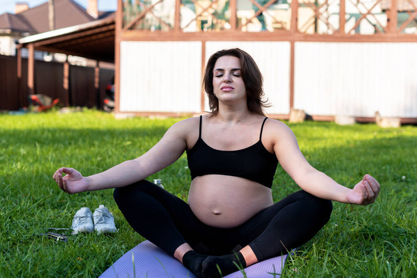 Terhes nő jógázik és füvön meditál az udvaron, mély levegőt szívva, a jóga lótusz kényelmesen pózol. Jóga Anyaság, mentális egészség és terhes fogantatás. - Fotó, kép