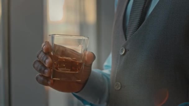 Cropped shot of unrecognizable African American businessman shaking glass of whiskey while thinking about work - Materiaali, video