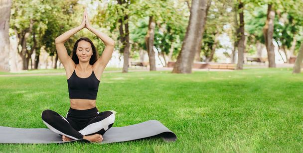 Genç esmer, beyaz kadın parkta egzersiz yaparken yoga yapıyor. Sağlıklı bir yaşam tarzı. Doğada fiziksel egzersiz. Parkta meditasyon yapan bir kız. Web pankartı, boşluğu kopyala - Fotoğraf, Görsel