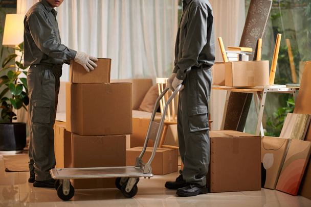 Movers putting cardboard boxes on moving cart when loading van - Photo, Image