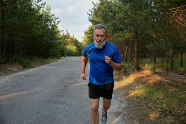 Старший бежит по проселочной дороге. Здоровый образ жизни и физическая активность для здоровья после выхода на пенсию - Фото, изображение