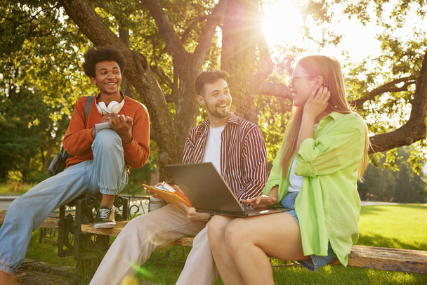 Magabiztos mosolygós egyetemisták beszélgetnek egymással, miközben a szabadtéri kampusz parkjában pihennek. Szép beszélgetés a nemzetközi Millenniumi Emberek Csoportjával - Fotó, kép