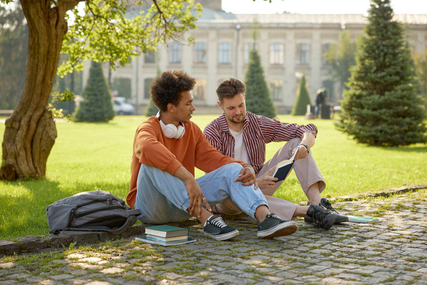 Два молодых студента разговаривают друг с другом, обсуждая идеи во время подготовки к университетским занятиям на открытом воздухе - Фото, изображение