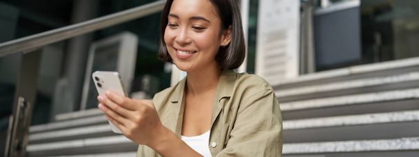 Portret van Aziatisch meisje neemt selfie op mobiele telefoon. Koreaanse vrouw glimlachen, video chat op smartphone app terwijl zit buiten op de trap. - Foto, afbeelding