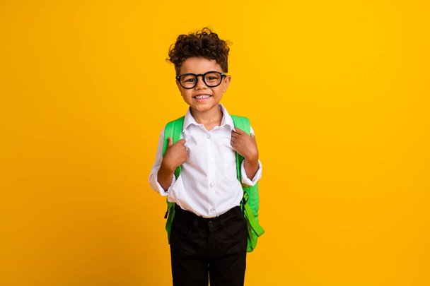 Photo of toothy beaming schoolboy with curly hairdo dressed white shirt in eyewear go to school isolated on yellow color background. - Foto, Bild