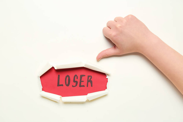 Woman showing thumb-down and word LOSER visible through hole in white paper - Photo, Image