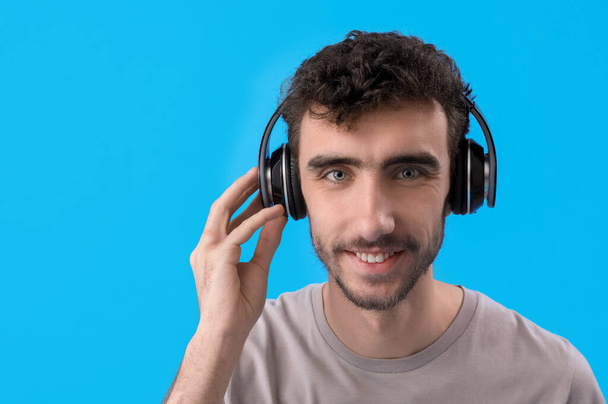 jong brunette man in hoofdtelefoon op blauwe achtergrond, close-up - Foto, afbeelding