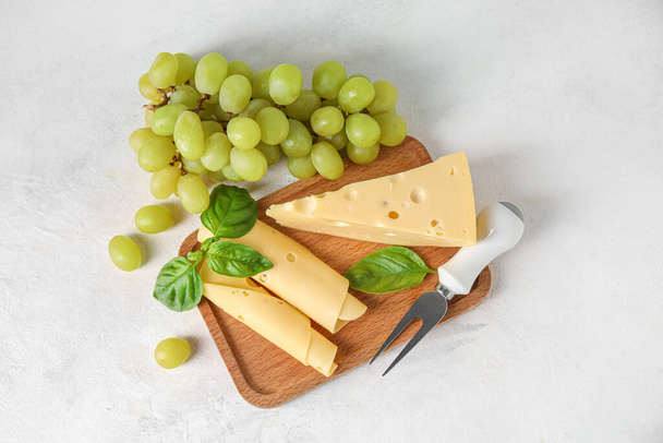Puinen kartonki maukkaita sveitsiläisiä juustoja ja viinirypäleitä kevyellä taustalla - Valokuva, kuva