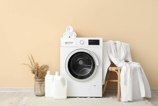 Máquina de lavar roupa, banquinho com roupão de banho e garrafas de detergente perto da parede bege - Foto, Imagem