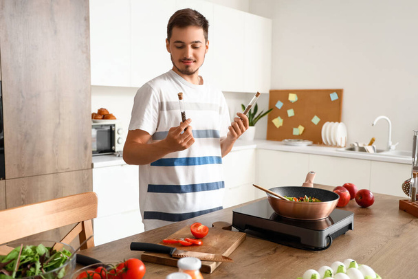 Молодой человек со специями жарит овощи на кухне - Фото, изображение