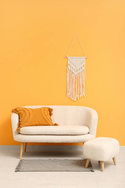 Уютный белый диван и оттоман у оранжевой стены с плетеным декором - Фото, изображение