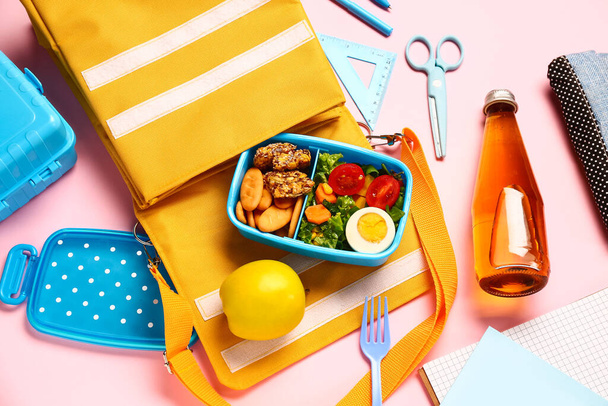 Rugzak, briefpapier, fles limonade en lunchbox met lekker eten op roze achtergrond - Foto, afbeelding