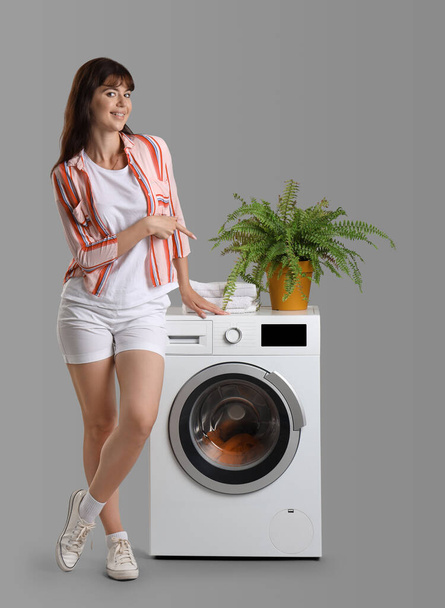 Молодая женщина указывает на стиральную машину на сером фоне - Фото, изображение