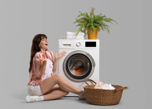 Удивленная молодая женщина со стиральной машиной на сером фоне - Фото, изображение