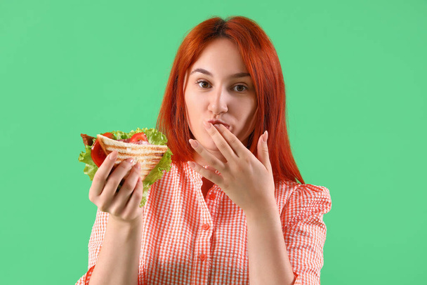 Junge rothaarige Frau isst leckeres Sandwich auf grünem Hintergrund, Nahaufnahme - Foto, Bild