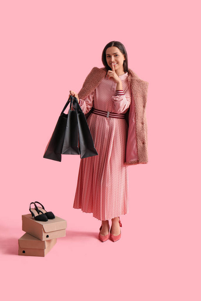 Mooie jonge vrouw met boodschappentassen en kartonnen dozen met stil gebaar op roze achtergrond. Zwarte vrijdag verkoop - Foto, afbeelding