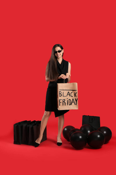 Kaunis nuori nainen ostoskassit ja ilmapallot punaisella taustalla. Musta perjantai myynti - Valokuva, kuva