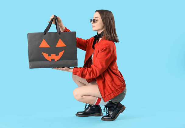 Mujer joven con bolsa de regalo de Halloween sobre fondo azul - Foto, imagen