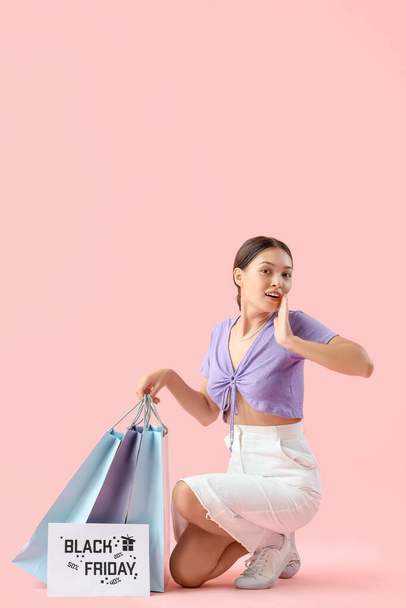 Surprised young Asian woman with shopping bags on pink background. Black Friday sale - Fotoğraf, Görsel