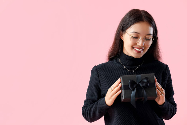ピンクの背景に贈り物を持ったアジアの若い女性. ブラックフライデーセール - 写真・画像