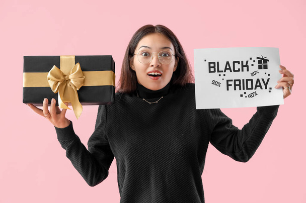 Překvapená mladá asijská žena s dárkem na růžovém pozadí. Černý pátek prodej - Fotografie, Obrázek