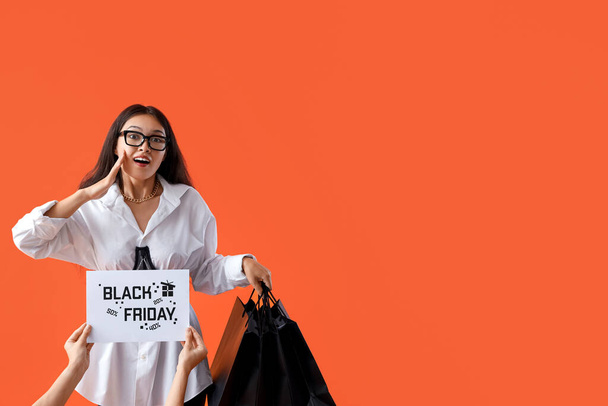 Surprise jeune femme asiatique avec des sacs à provisions sur fond orange. Vente Black Friday - Photo, image