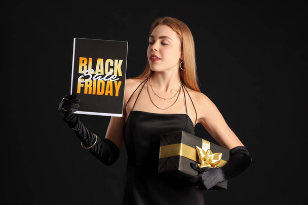 Молода жінка з листівкою і подарунком на темному тлі. Чорна п'ятниця продаж - Фото, зображення