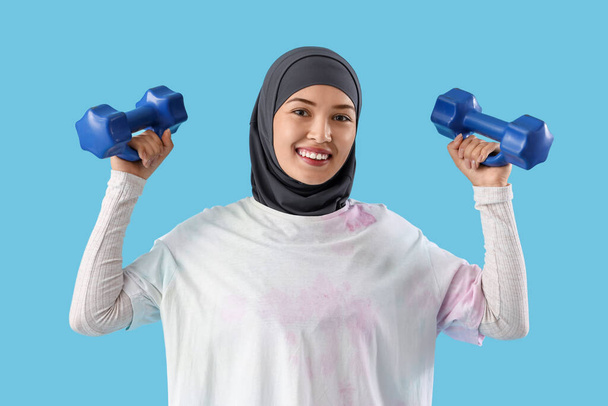 Urheilullinen musliminainen, jolla on käsipainot sinisellä taustalla - Valokuva, kuva