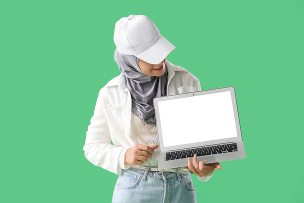 Mujer musulmana joven con portátil sobre fondo verde - Foto, imagen