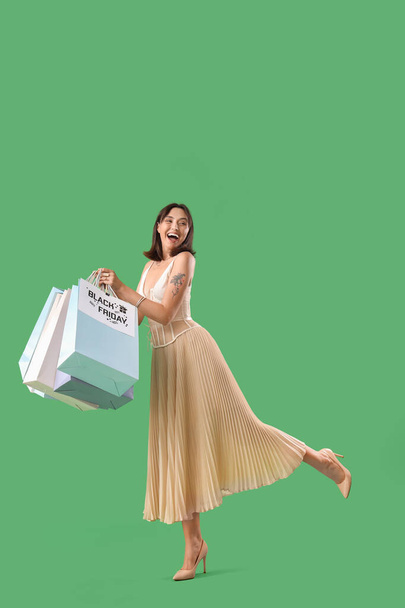 Mujer joven con bolsas de compras sobre fondo verde. Viernes Negro venta - Foto, Imagen