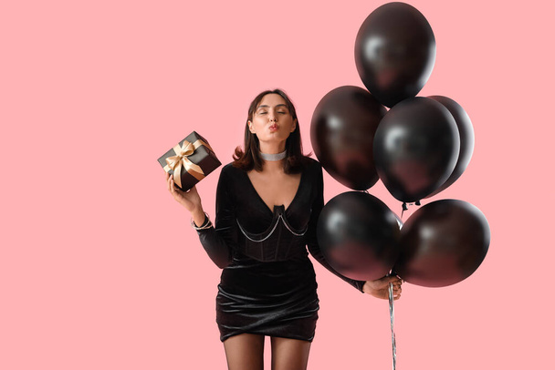 Mladá žena s dárkem a balónky foukání polibek na růžové pozadí. Černý pátek prodej - Fotografie, Obrázek