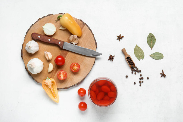 Tarro de tomates en escabeche y tablero de madera con diferentes especias sobre fondo blanco - Foto, Imagen