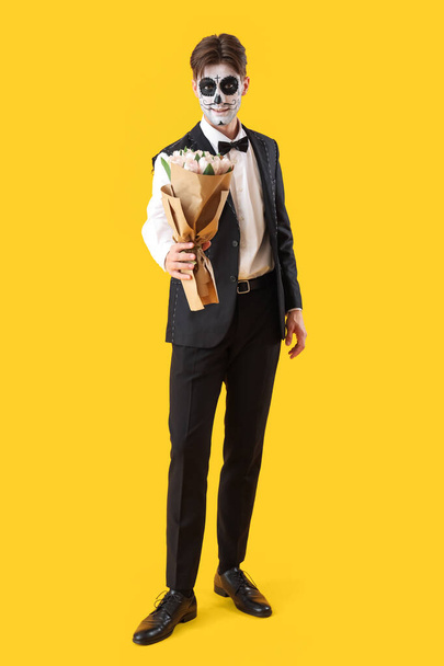 黄色の背景に花束のハロウィーンのために服を着た若い男 - 写真・画像
